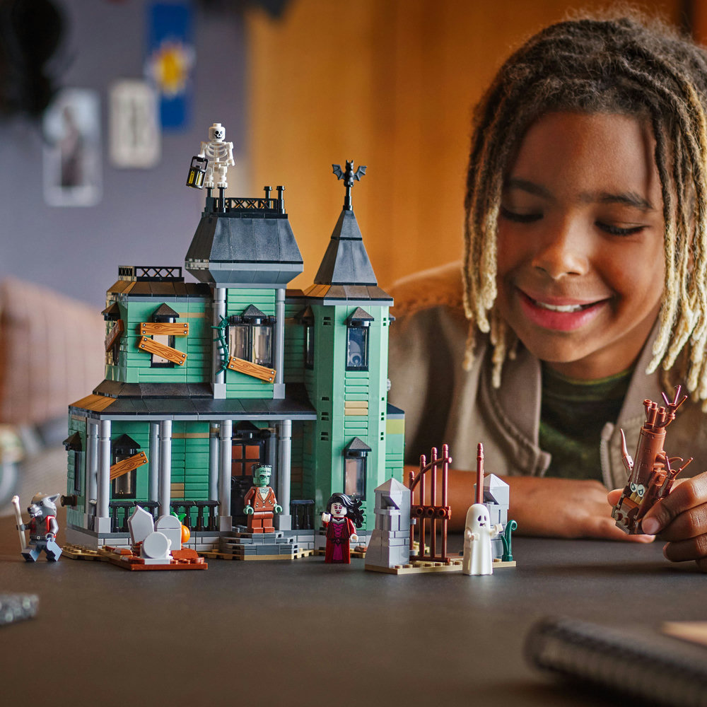 Child playing with a LEGO Creator: 3-in-1 Haunted Mansion House set on a table.