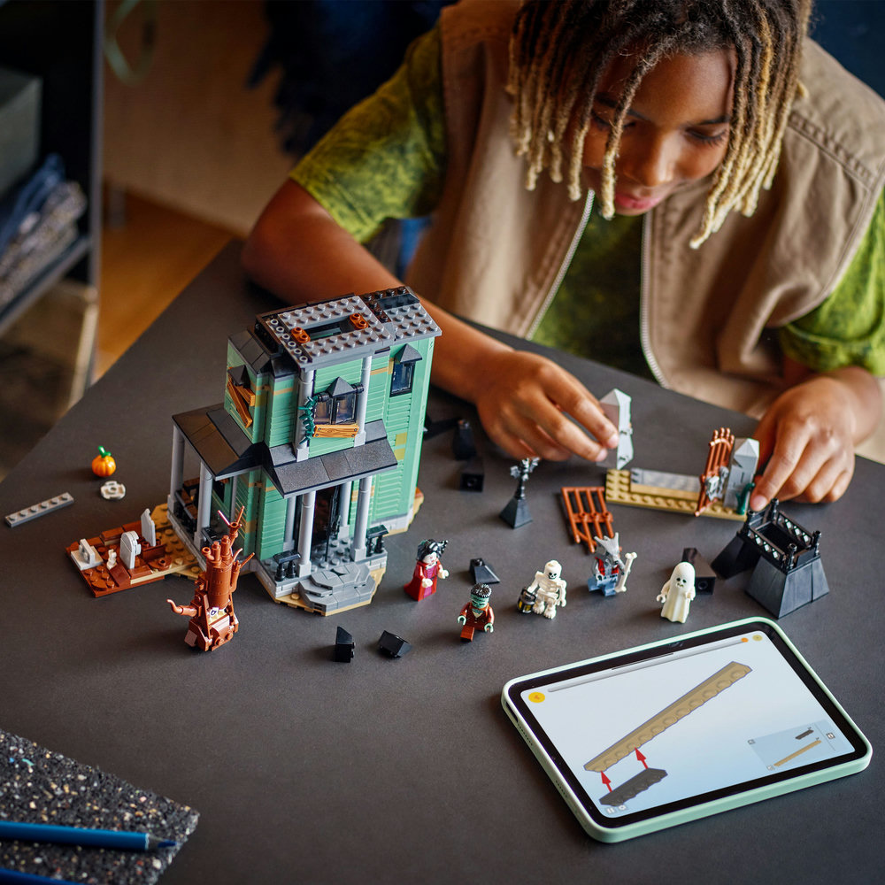 Child playing with a lego haunted house set on a table with a tablet displaying a game.