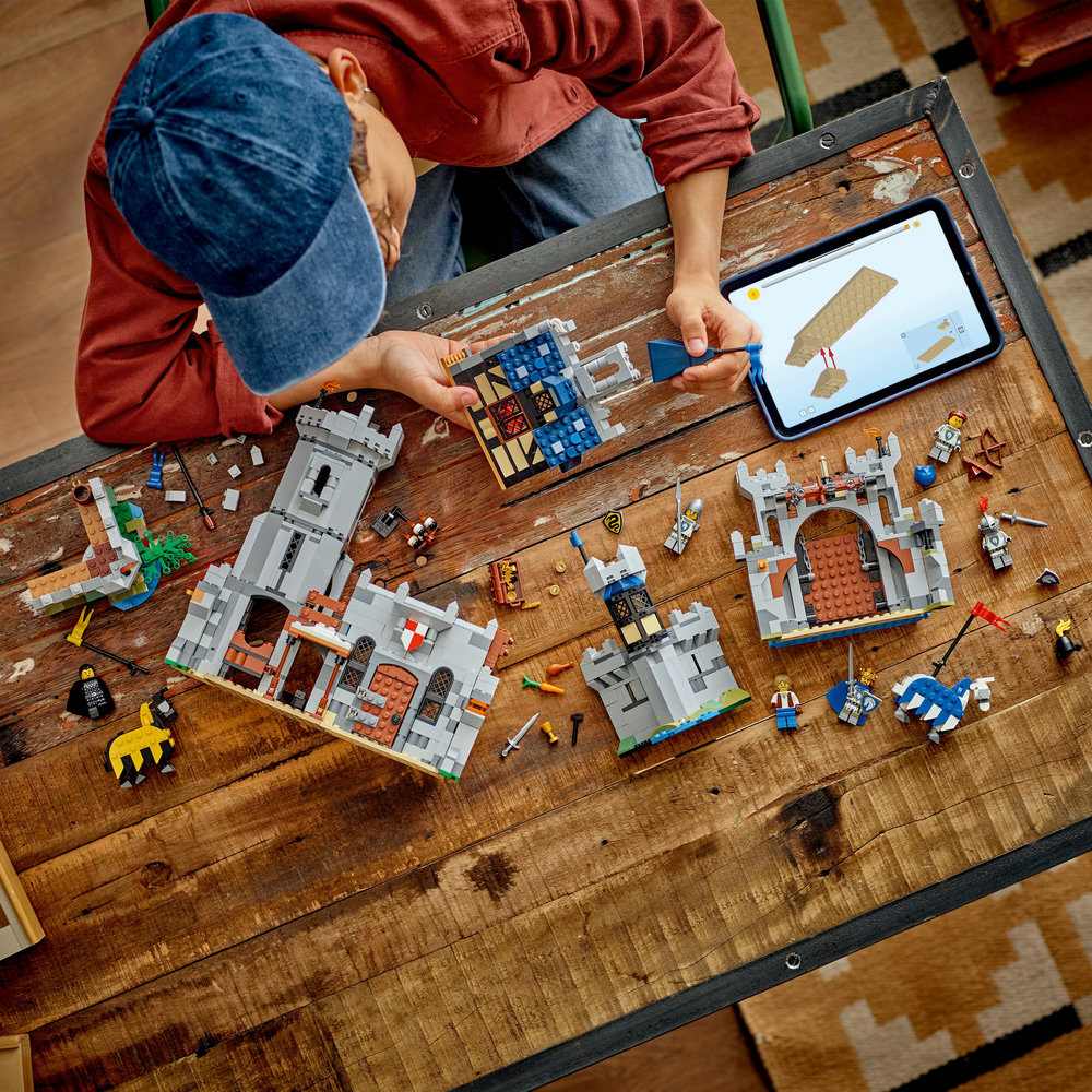Child building a LEGO castle set on a wooden table.