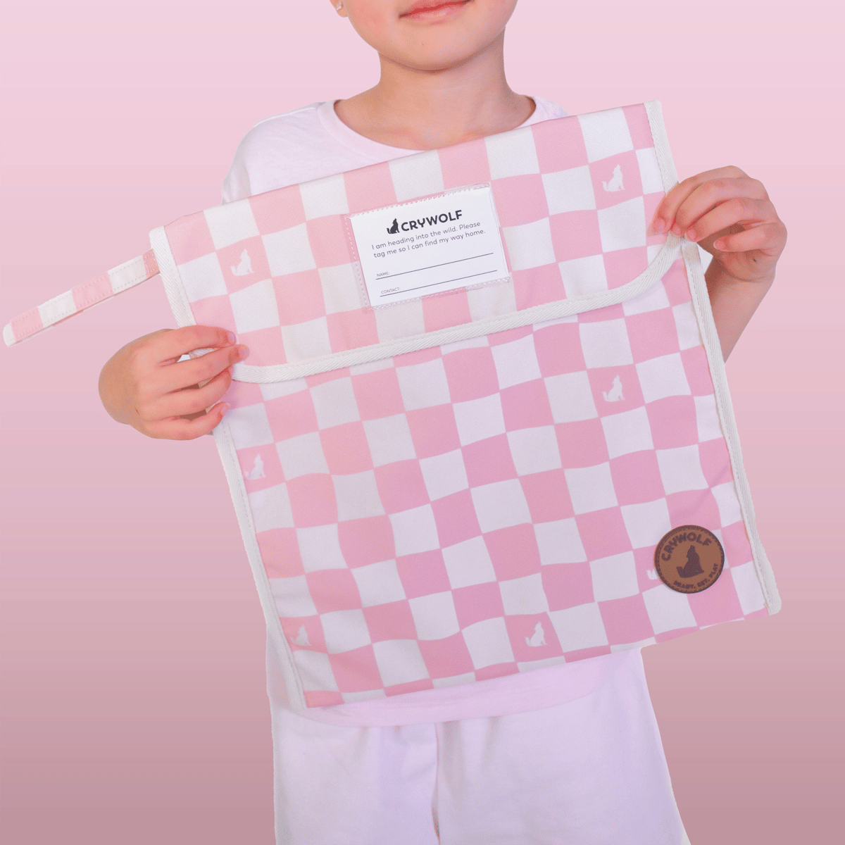Person holding a pink and white checkered bag with a visible brand label against a pink background
