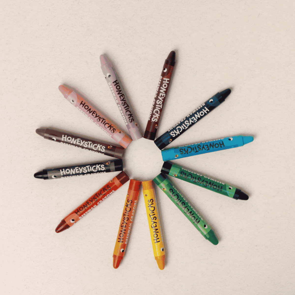 Colorful 'Honeysticks' crayons arranged in a circular pattern on a beige background.