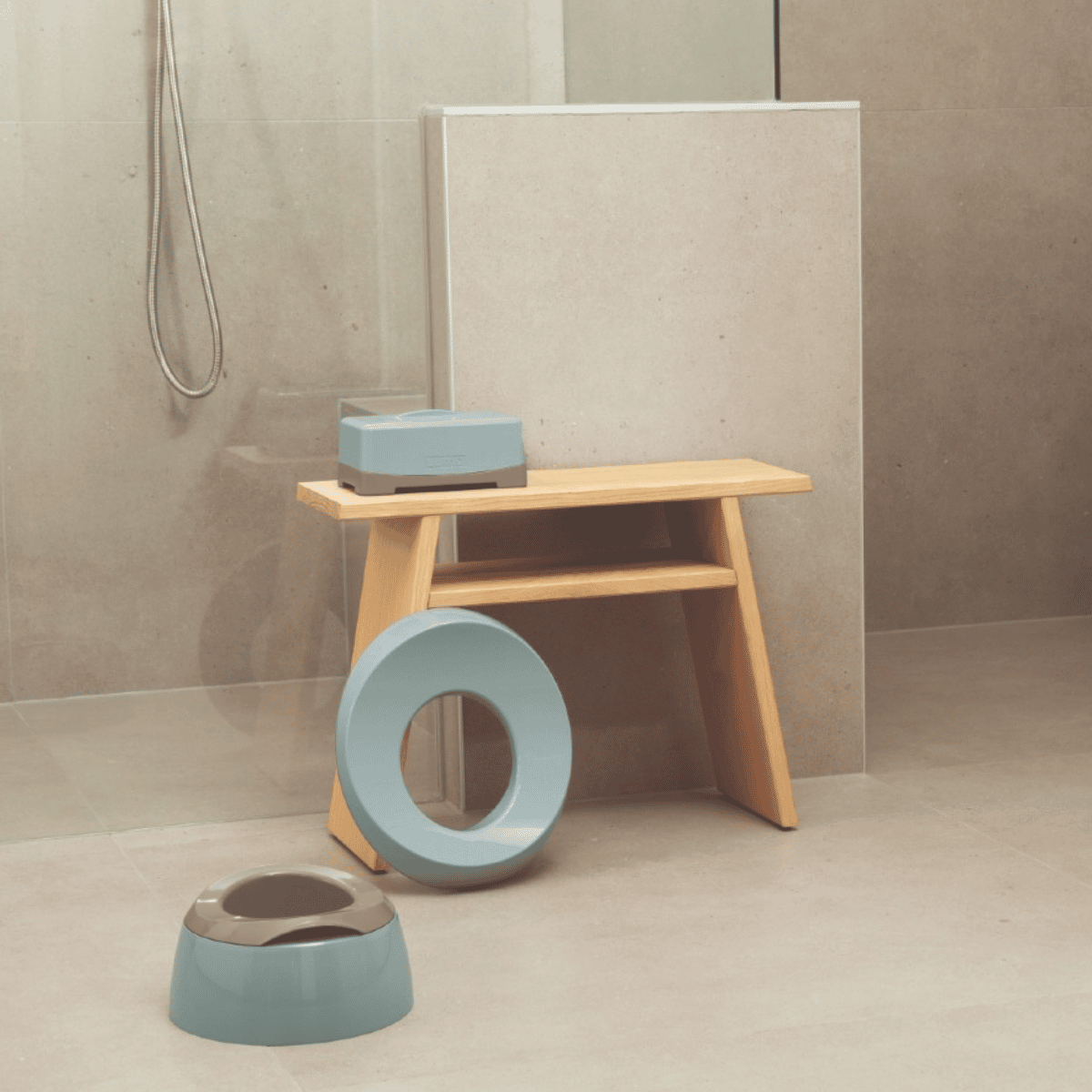 A minimalist bathroom scene with a light wood stool, a light blue ring-shaped toilet lid, and a matching light blue toilet bowl on a beige tiled floor.