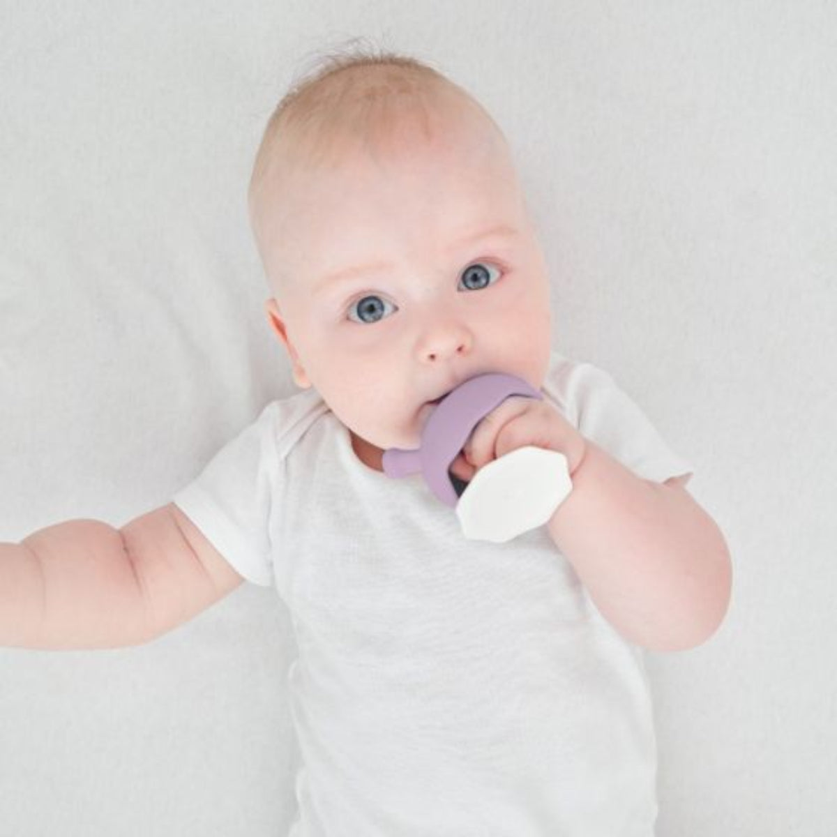 Baby holding a purple and white teether against a plain background