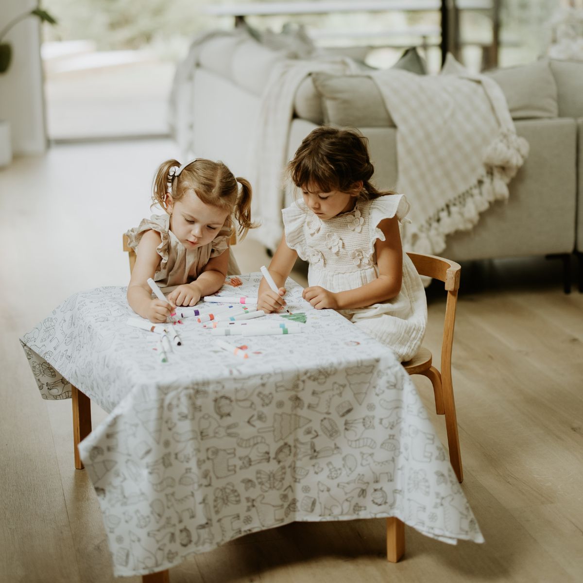 Two girls colouring in the Colour Me Kids Tablecloth at the table on a playdate.