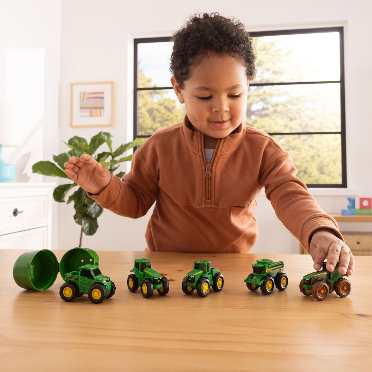 Child playing with John Deere toy tractors on a wooden table
