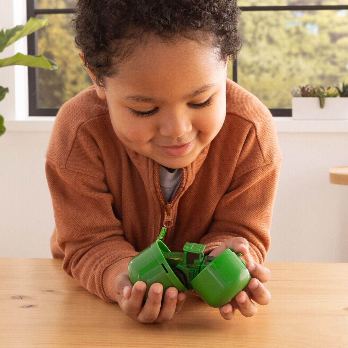 Child playing with a green John Deere toy car indoors