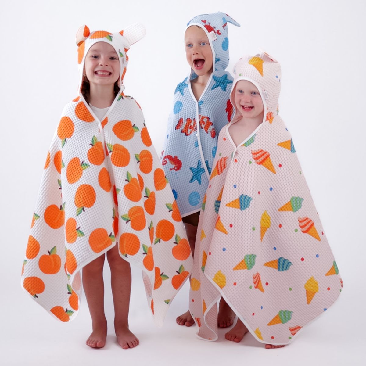 Three children wearing colourful hooded towels with animal designs on a white background