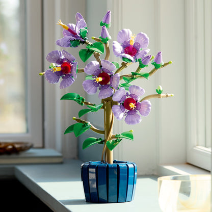 Decorative flower arrangement with purple LEGO flowers in a blue pot on a windowsill.