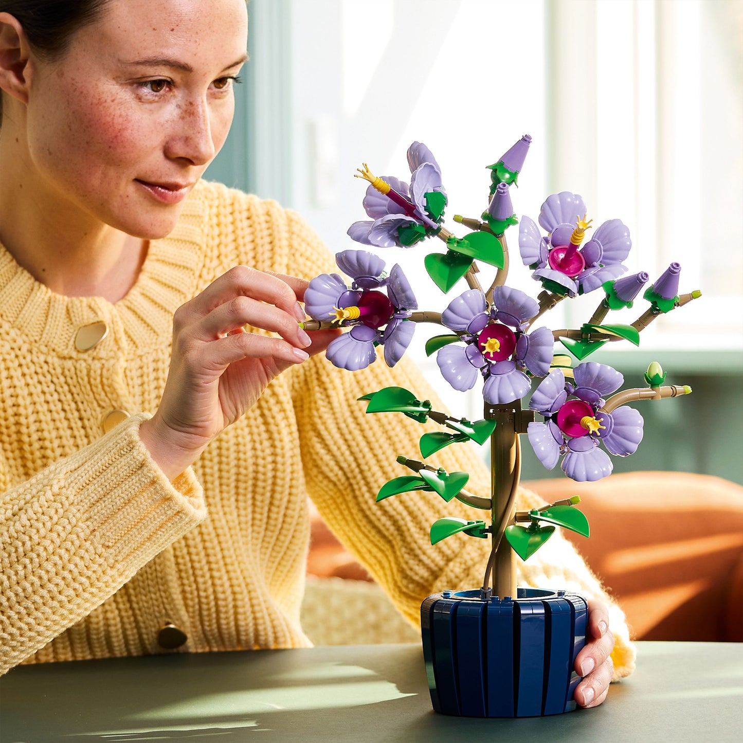 Woman holding a small potted plant with LEGO flowers indoors