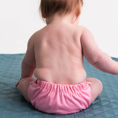 Baby wearing a pink diaper sitting on a textured blue surface.