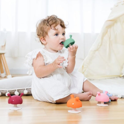 Baby playing with a green toy on a wooden floor with colorful toys around