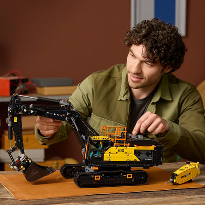 Man playing with a LEGO Technic: Volvo EC500 Hybrid Excavator on a wooden table