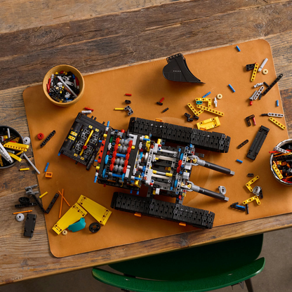 LEGO Technic: Volvo EC500 Hybrid Excavator set pieces on a brown mat with a wooden table background