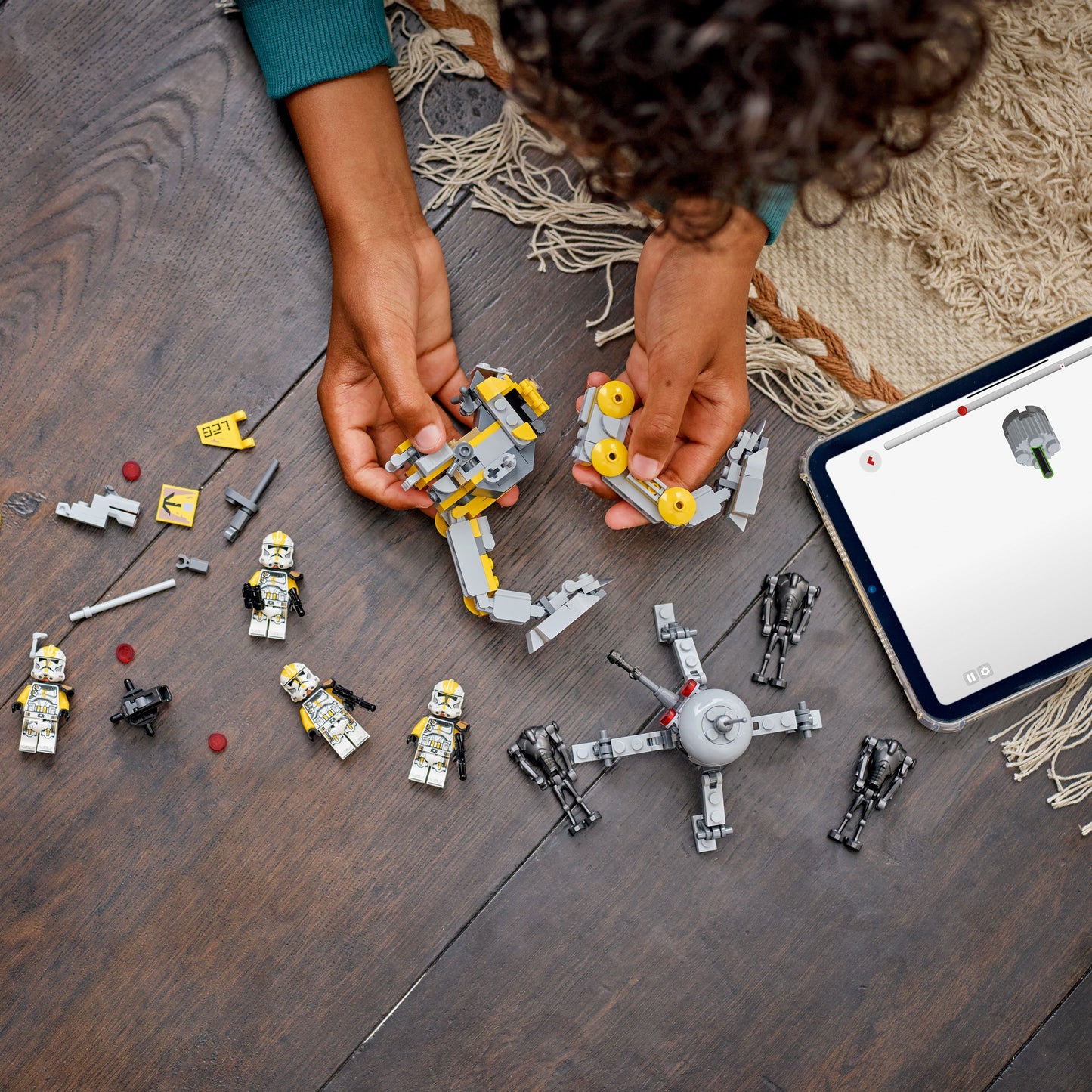 Child playing with toy building blocks on a wooden floor next to a tablet.
