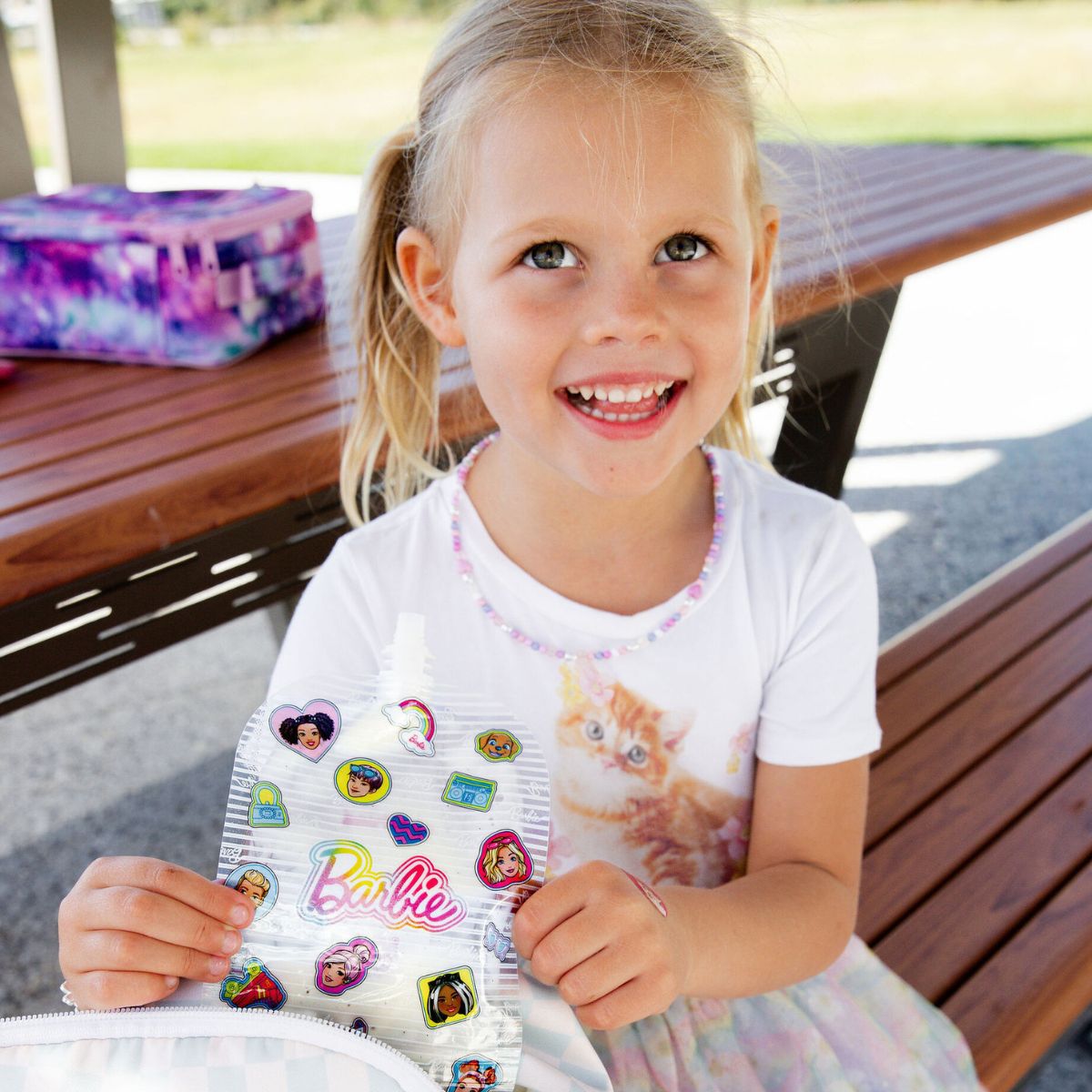 Young girl holding a Barbie-themed sticker book outdoors