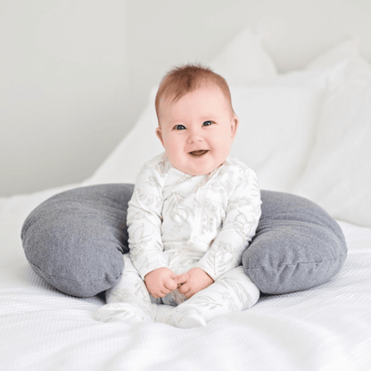 Baby sitting on a gray cushion with a white background