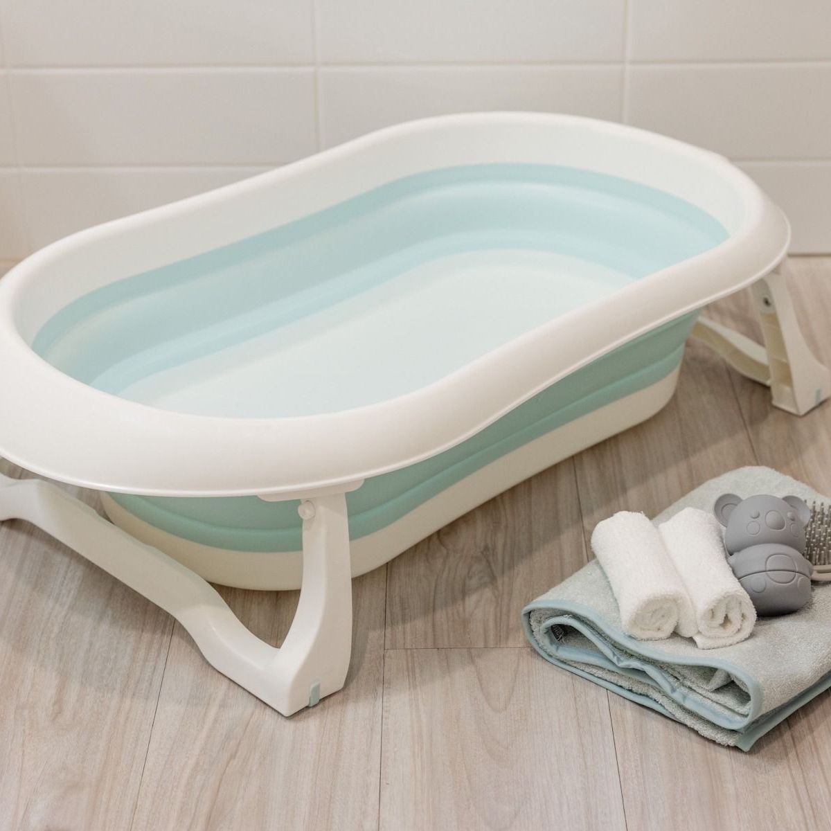 Foldable baby bath tub on a wooden floor with towels.