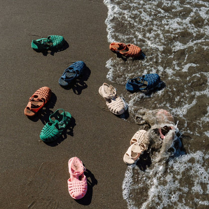 Colorful children's sandals on a sandy beach with waves.