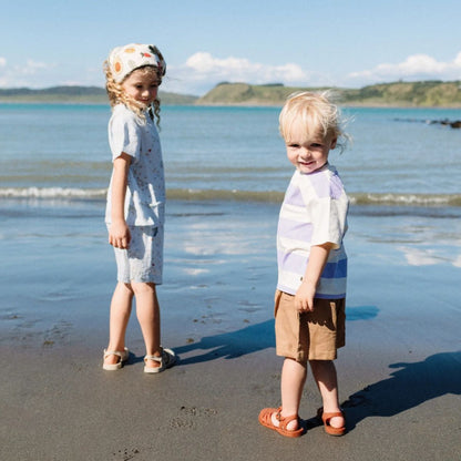Two children standing on a beach with ocean and sky in the background wearing jelly sandels.