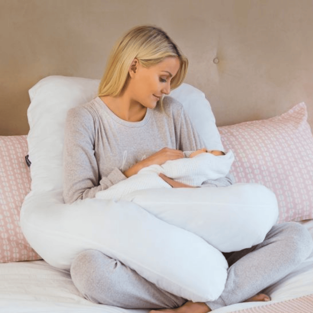 Woman holding a baby with a U-shaped body pillow on a bed