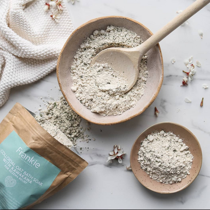 Bowl of bath soap powder with a wooden spoon and packaging on a marble surface.