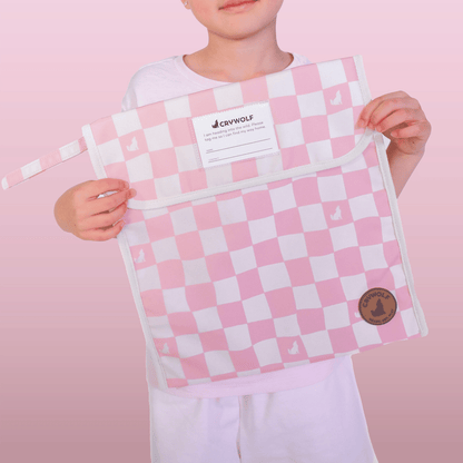 Person holding a pink and white checkered bag with a visible brand label against a pink background