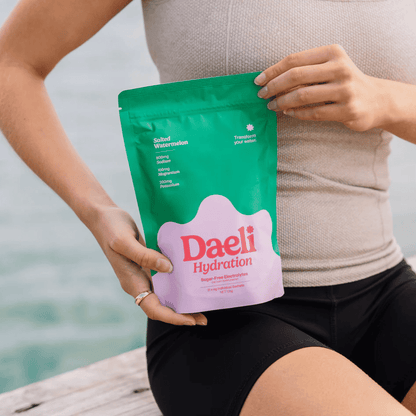 Person holding a green and pink Daeli Hydration package by a body of water.