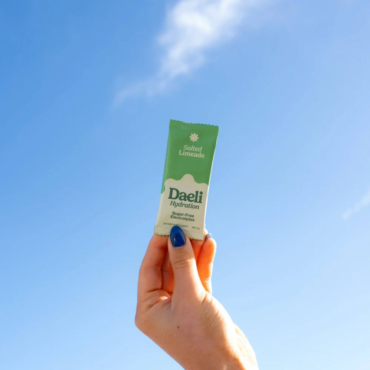 Hand holding a Daeli hydration packet against a blue sky