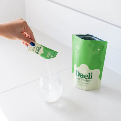 Person holding a green Daeli packaging over a white container on a white background