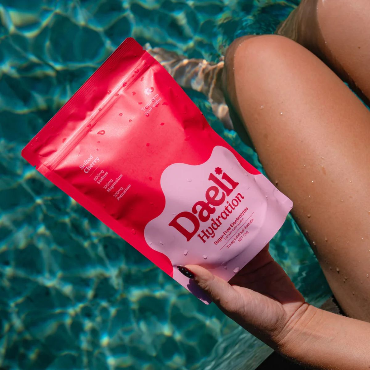 Person holding a pink 'Daeli Hydration' package by a pool