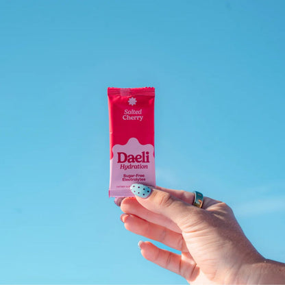 Hand holding a pink Daeli hydration package against a blue sky