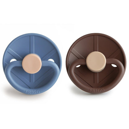 Two baby pacifiers, one blue and one brown, on a white background. Frigg is a Swedish Brand