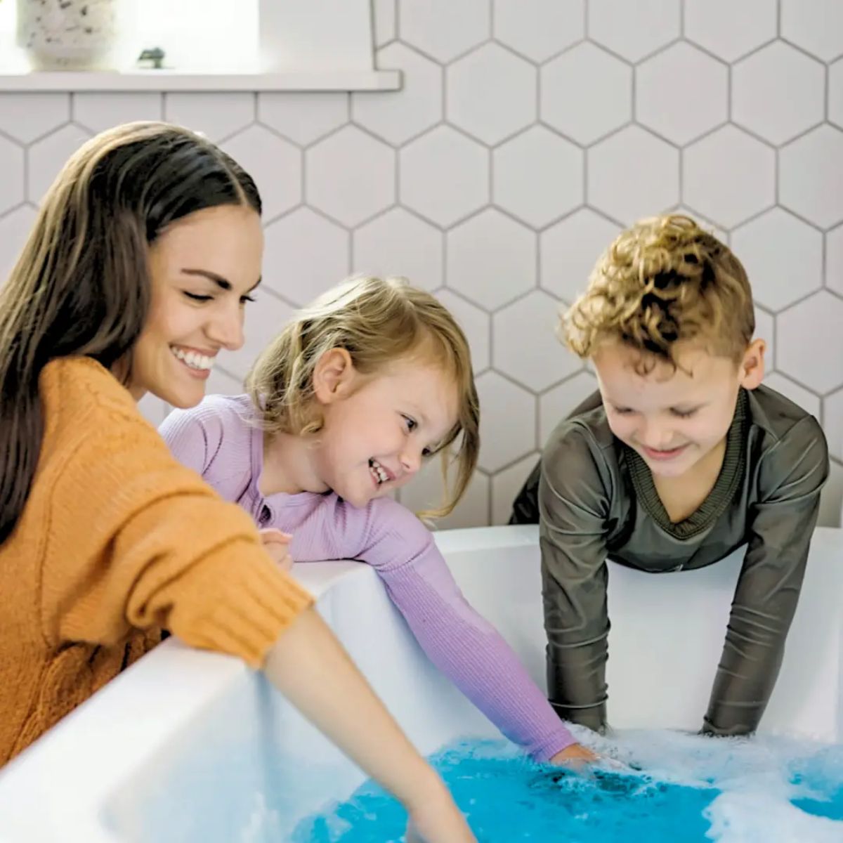 Woman and two children playing with blue bubbles in a bathtub.