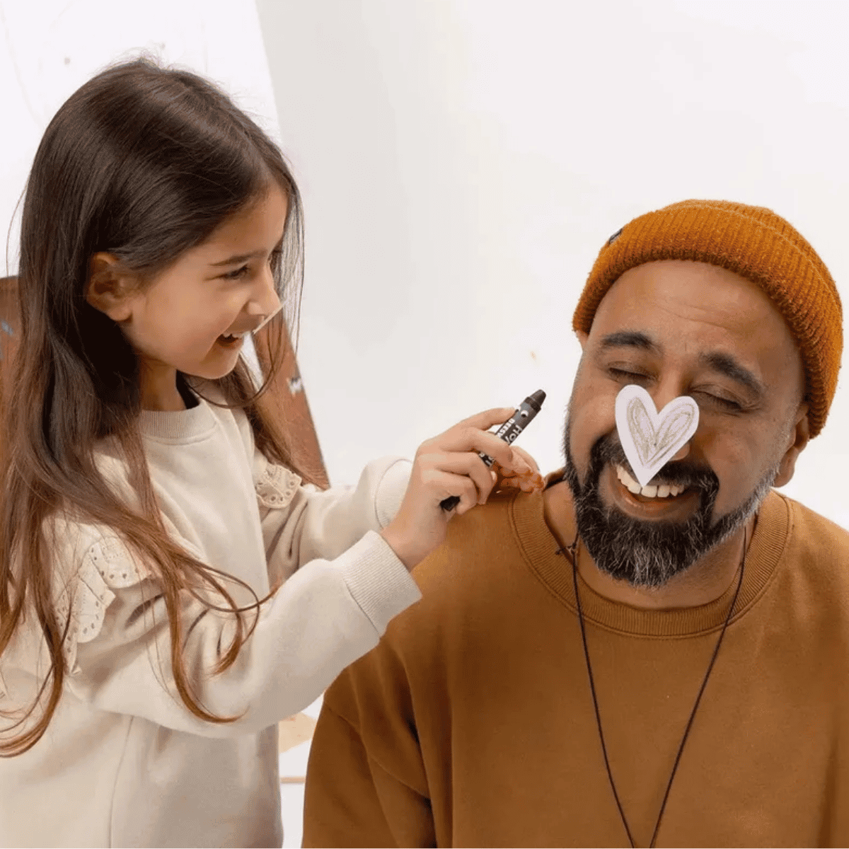 Child applying crayon to a man's face with a heart-shaped object.
