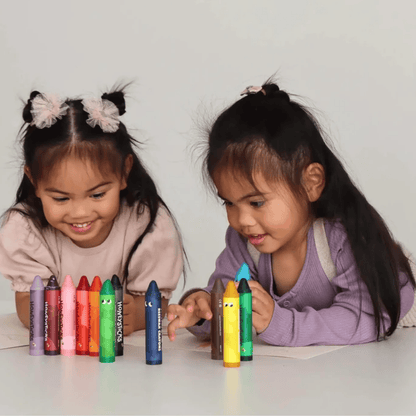 Two young girls playing with colorful crayons on a white surface.