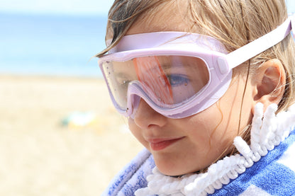 Child wearing goggles and a towel on a beach