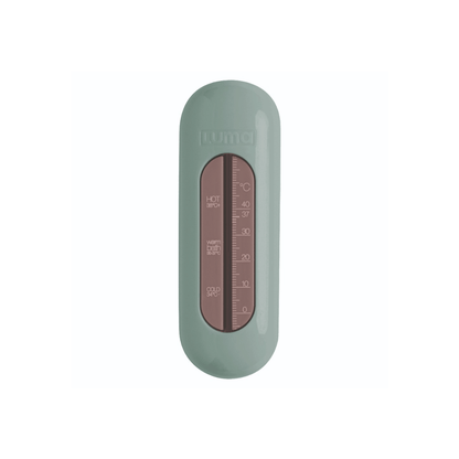 A LUMA bath thermometer with a sage green outer casing and a central brown glass window showing the temperature scale.