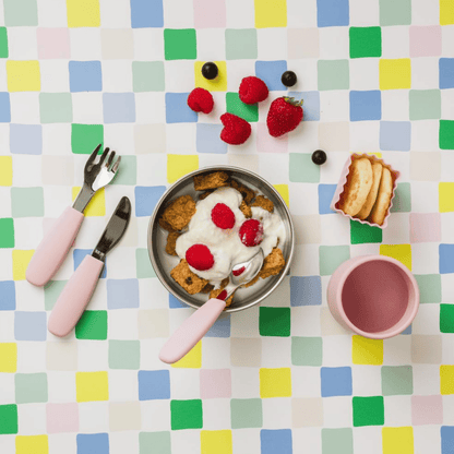 Breakfast setting with a bowl of cereal, yogurt, and berries on a colorful checkered tablecloth.