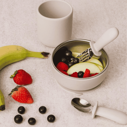 Metal bowl with fruit salad, white cup, and utensils on a light surface