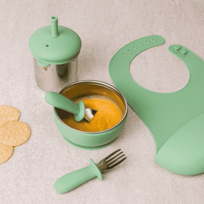 Green baby feeding set with bowl, spoon, bib, and fork on a light background