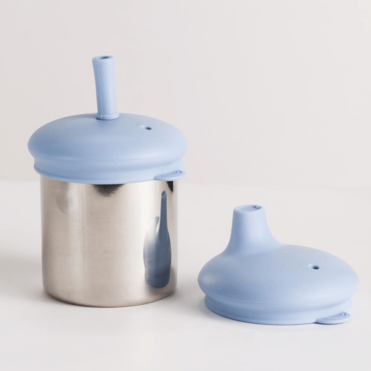 Stainless steel cup with a blue silicone lid and straw on a light gray background