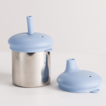 Stainless steel cup with a blue silicone lid and straw on a light gray background