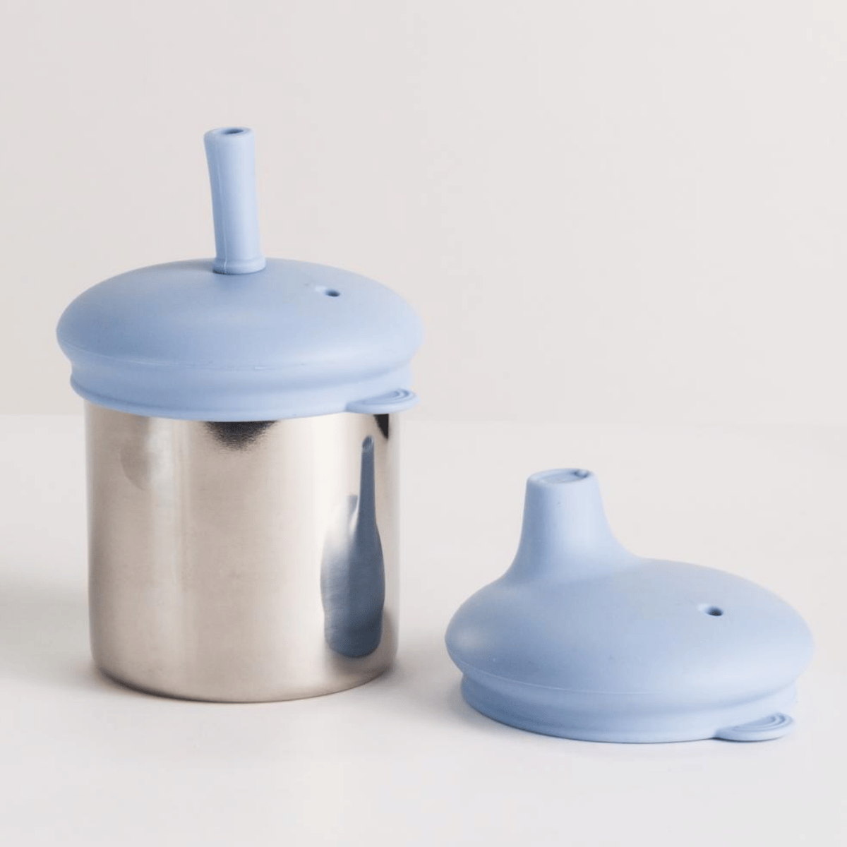 Stainless steel container with blue silicone lid and straw on a light gray background