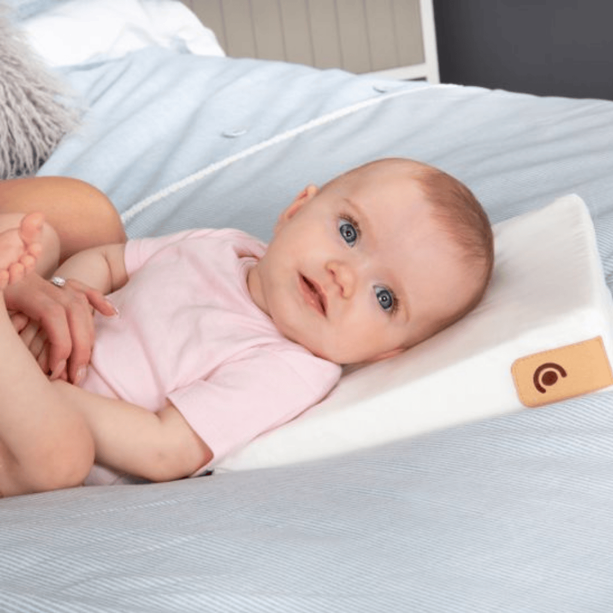 Baby lying on a white pillow with a leather tag on a bed