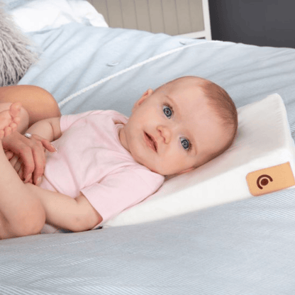 Baby lying on a white pillow with a leather tag on a bed