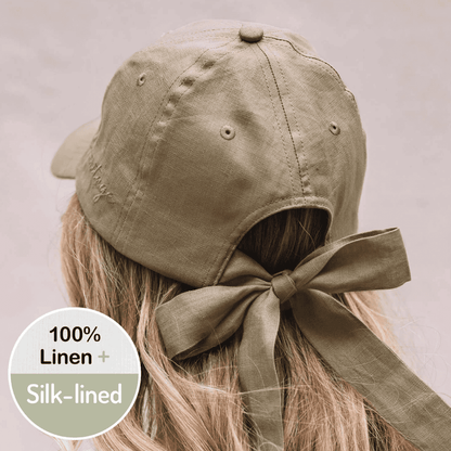 Khaki cap with a bow on a person's head, featuring 100% linen and silk-lining text.