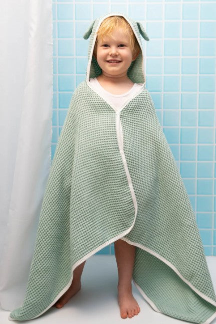 Child wrapped in a green hooded towel with a white border against a blue tiled wall.