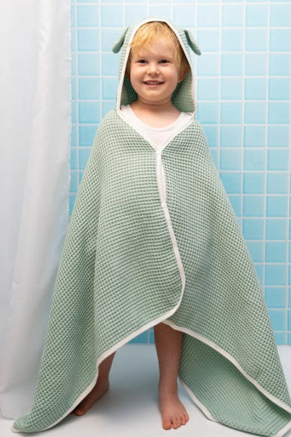 Child wrapped in a green hooded towel with a white border against a blue tiled wall.