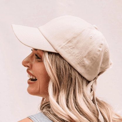 Woman wearing a beige cap with 'Heritage' embroidery on a light background