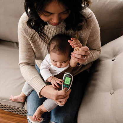 Woman holding a baby and a digital thermometer on a couch